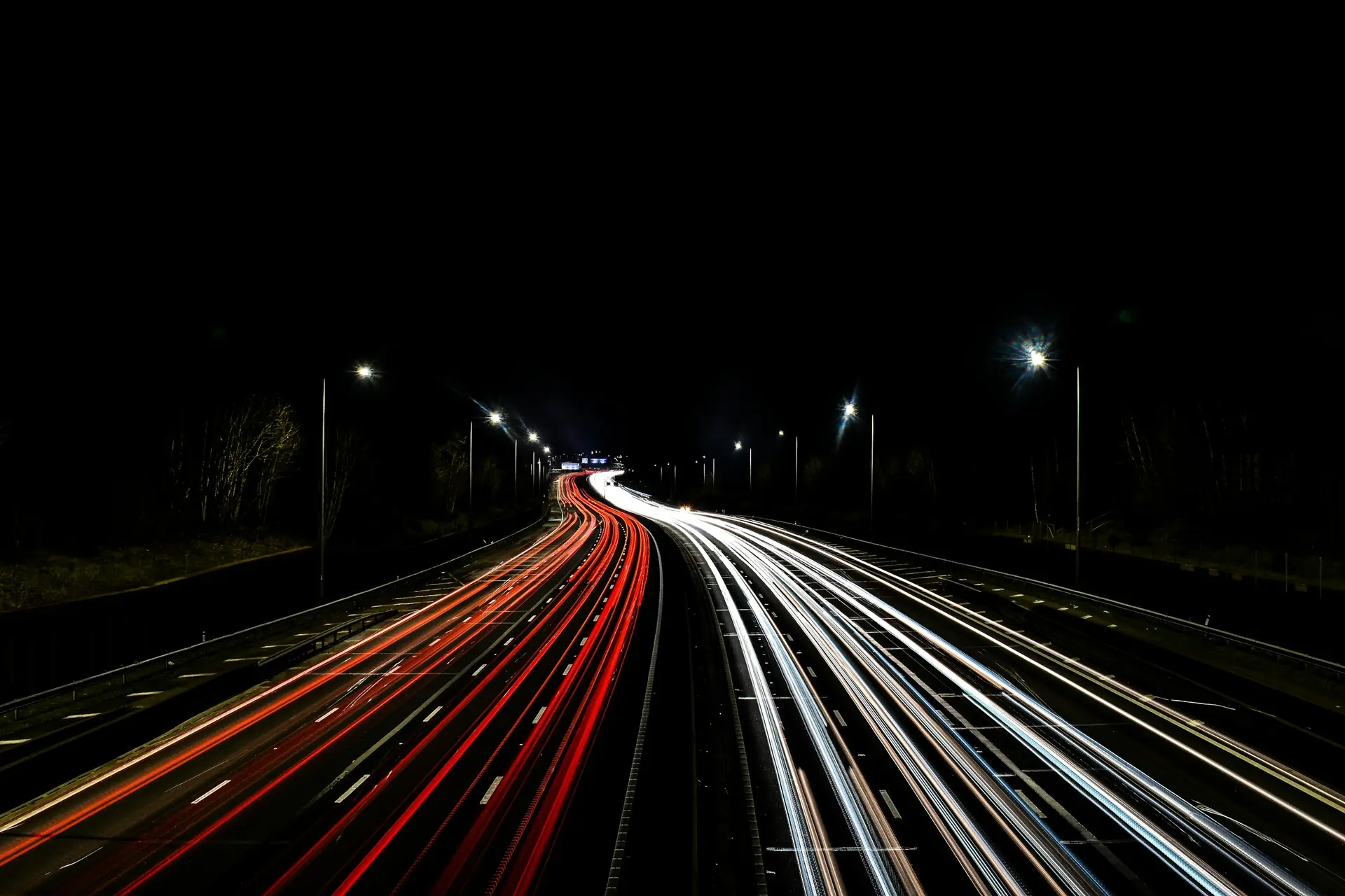 An empty highway at night, lit by streetlights and passing traffic.