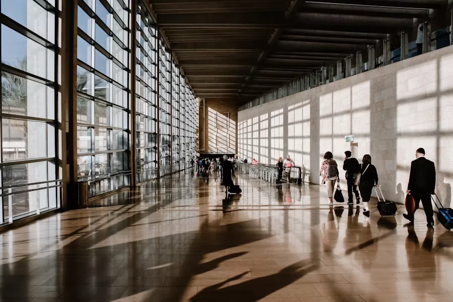 Travellers with luggage walking through a sunlit airport terminal.