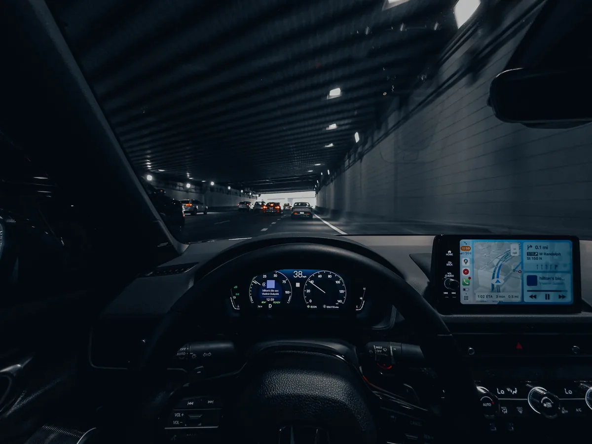 The view forward from inside a vehicle at night, instruments lit, city road ahead.
