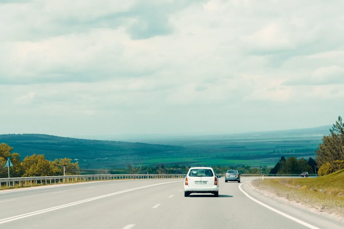 A white car on an open highway running between low hills.