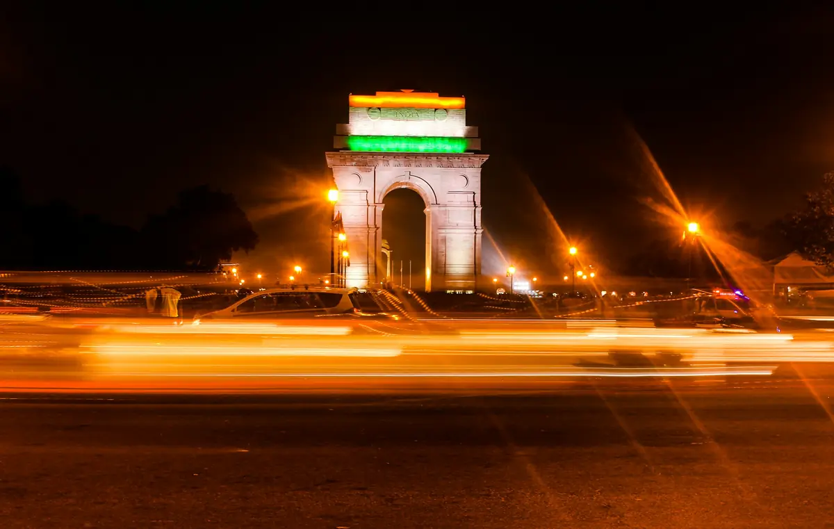 India Gate at night, framed by the light trails of passing traffic.