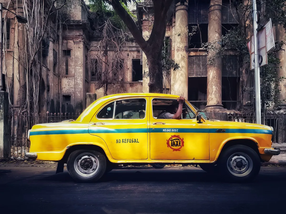 A yellow Ambassador taxi parked in front of a weathered colonial facade in Kolkata.