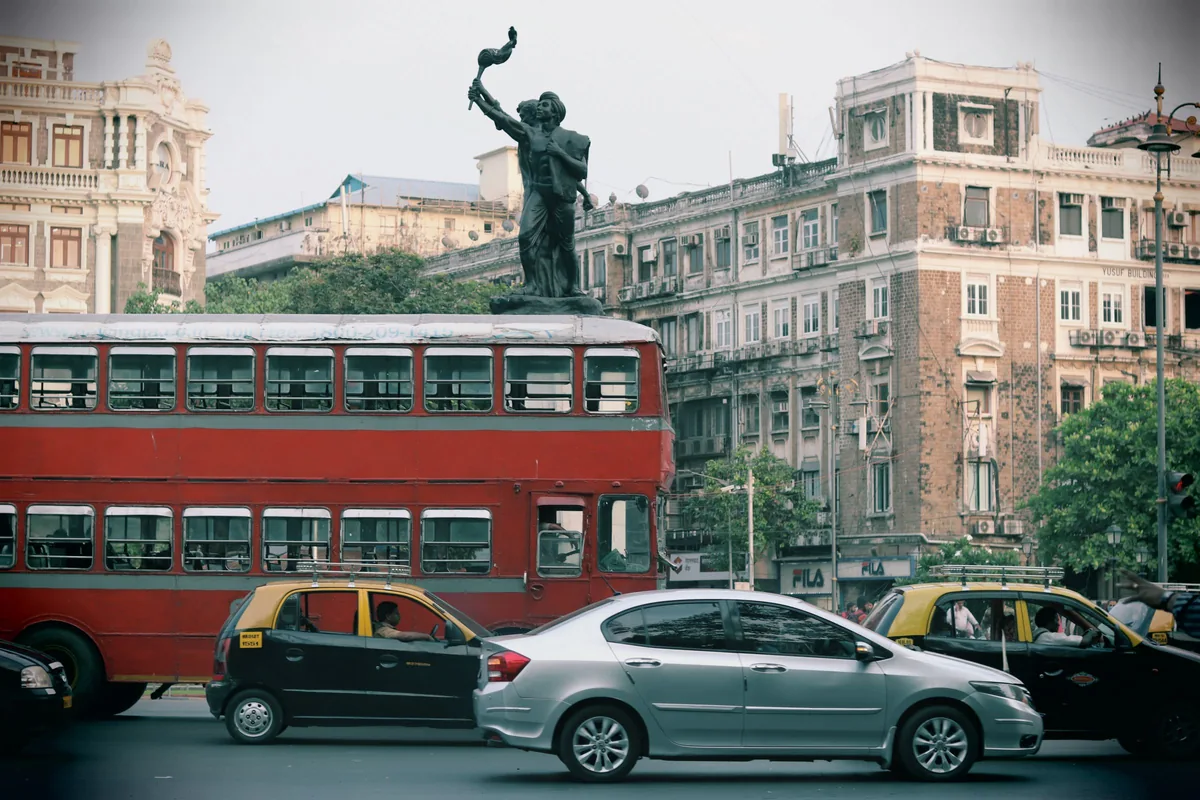 A busy Indian street with a red double-decker bus passing a monument.