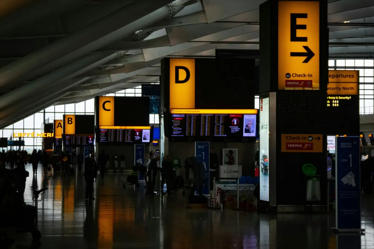 An airport concourse at night, gate signage lit above an almost empty floor.