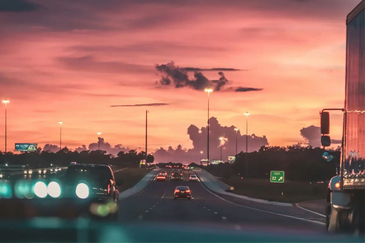 Traffic on a highway beneath a pink and orange evening sky.