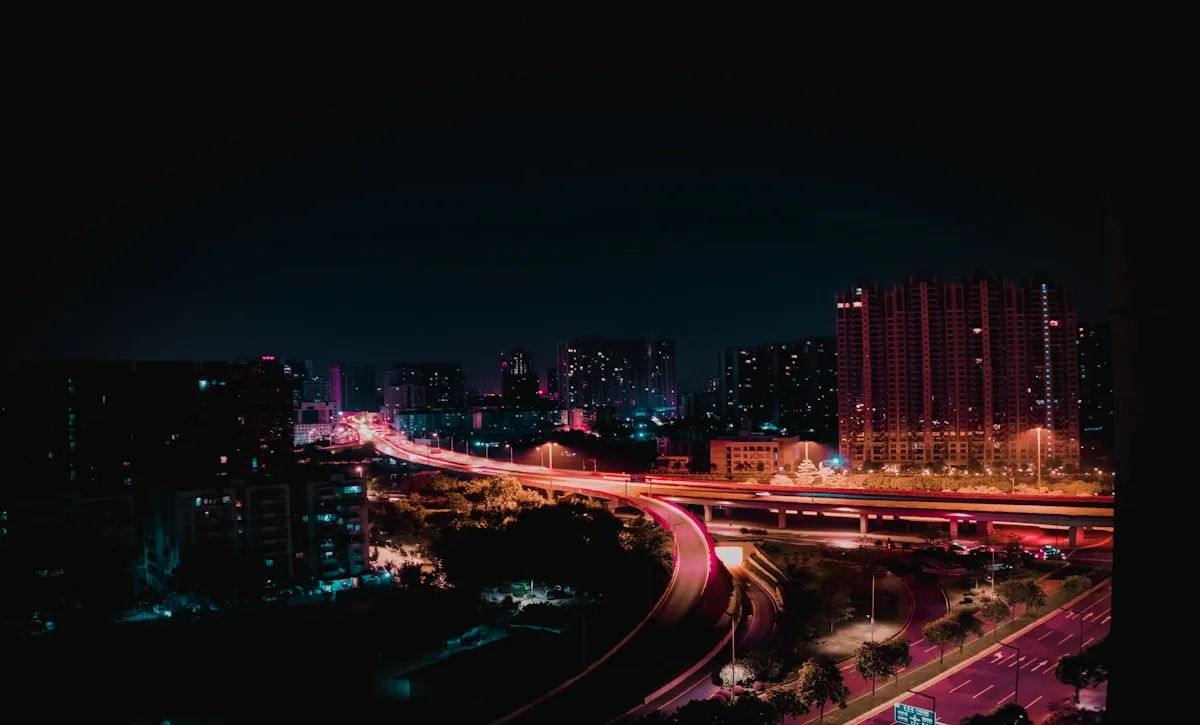 A city interchange at night, roads threading between lit towers.