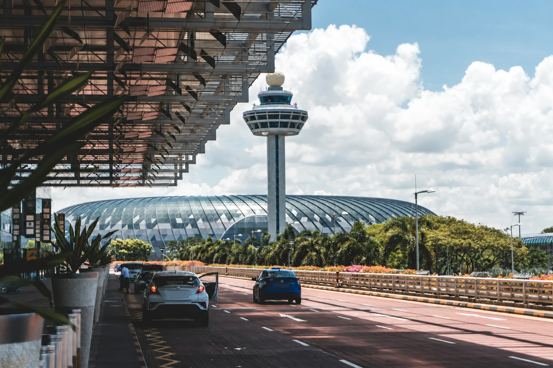 An airport approach road curving toward a terminal, with cars in the pick-up lane.
