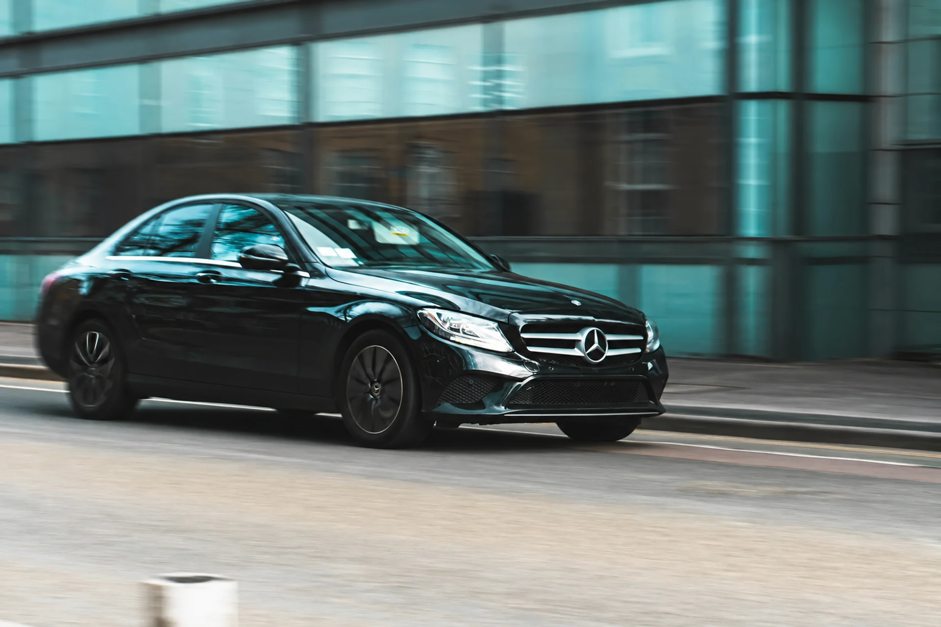 A dark executive sedan moving past a glass building, the background blurred with speed.