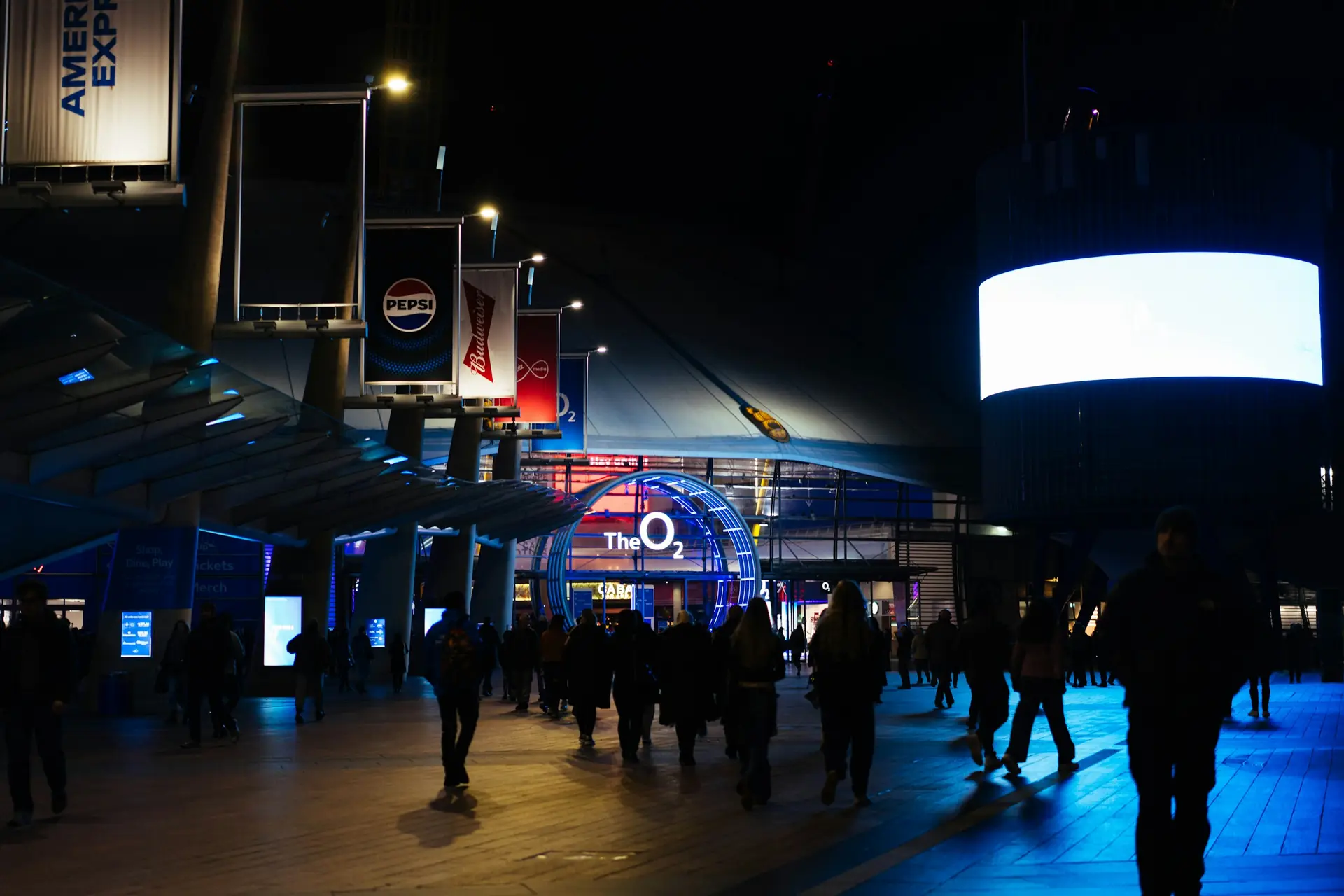 Guests arriving at a large venue at night under blue architectural lighting.