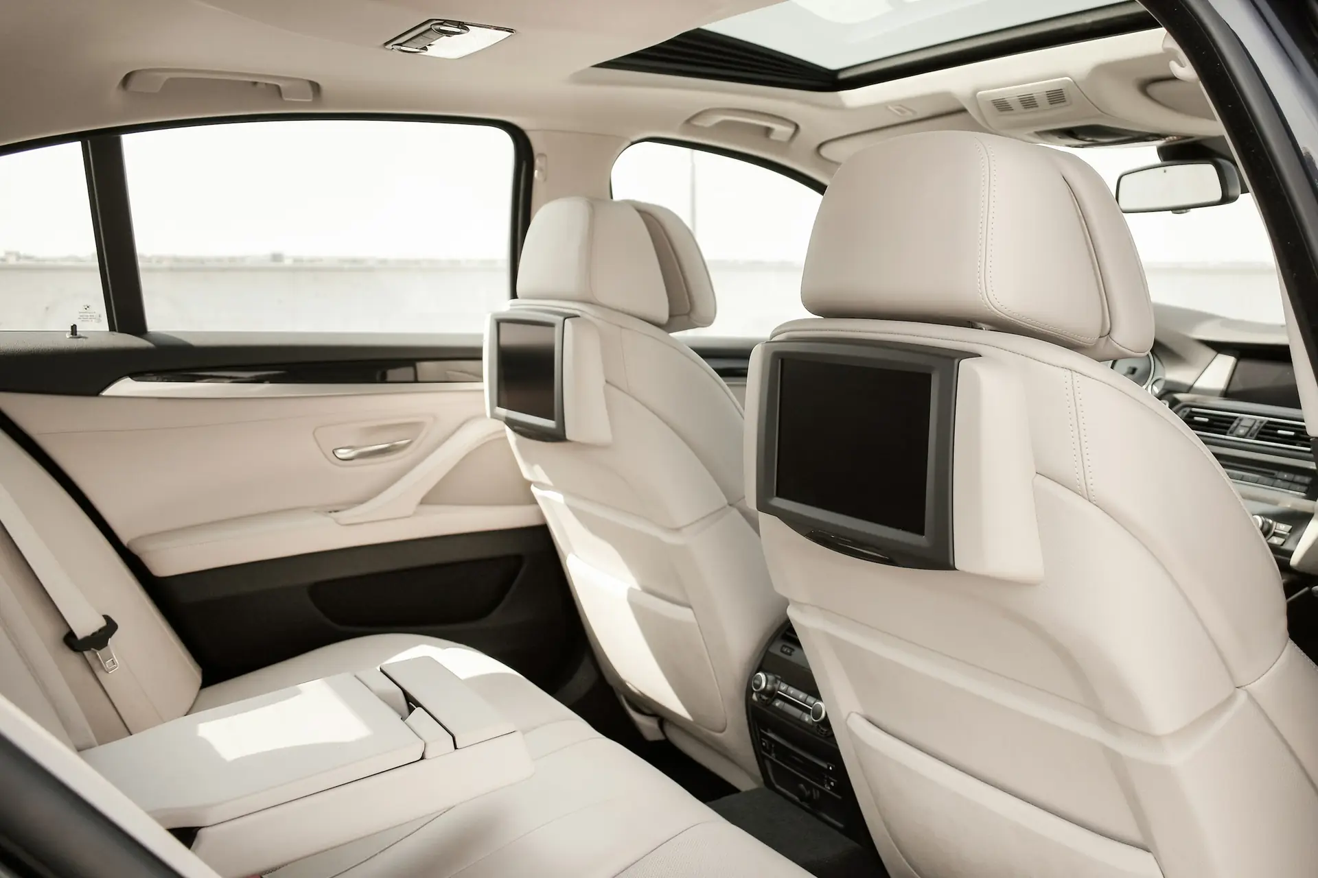 The rear cabin of an executive saloon, cream leather seats and rear screens.