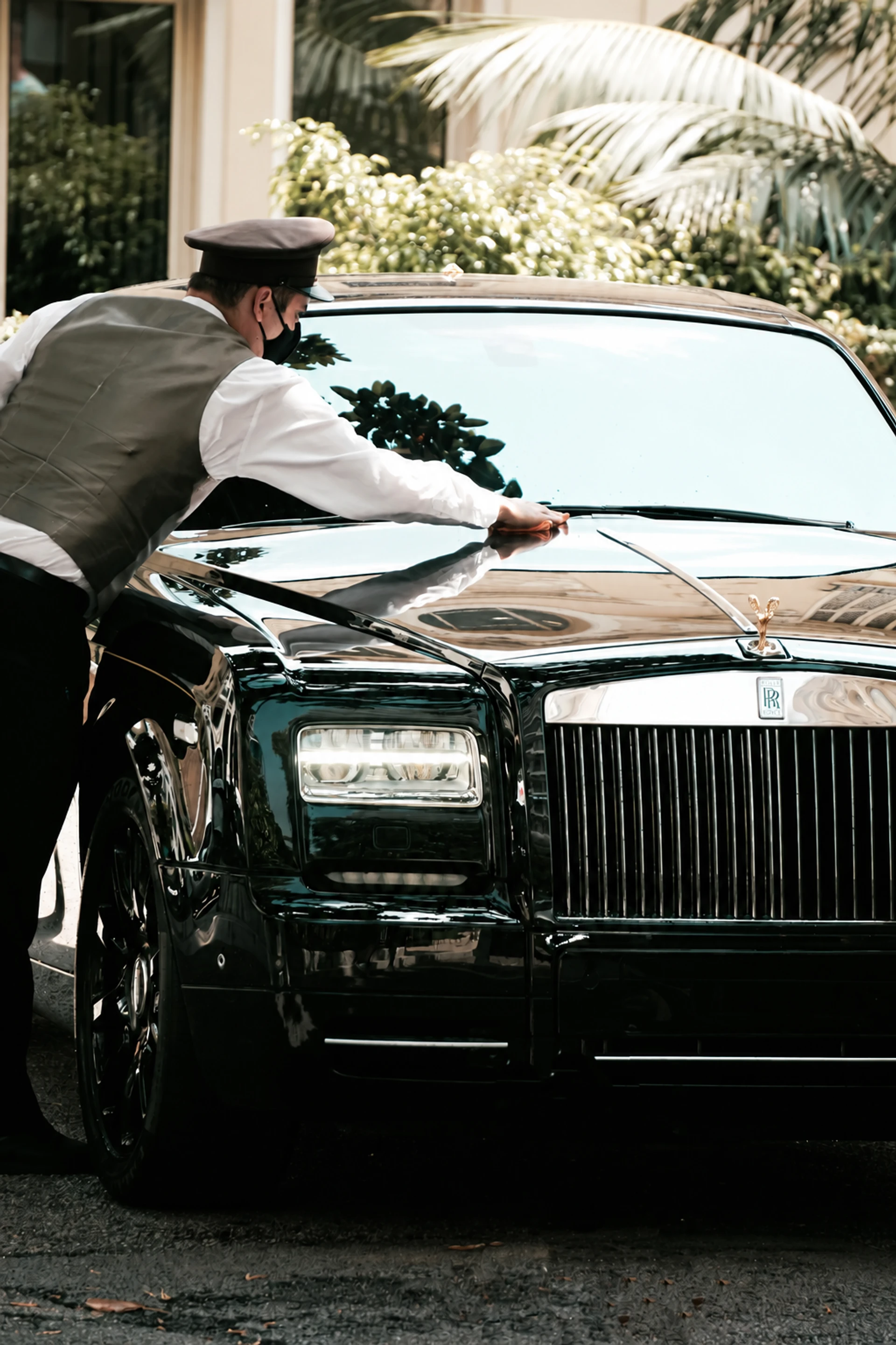 A uniformed chauffeur in white gloves finishing the last detail on a waiting car.