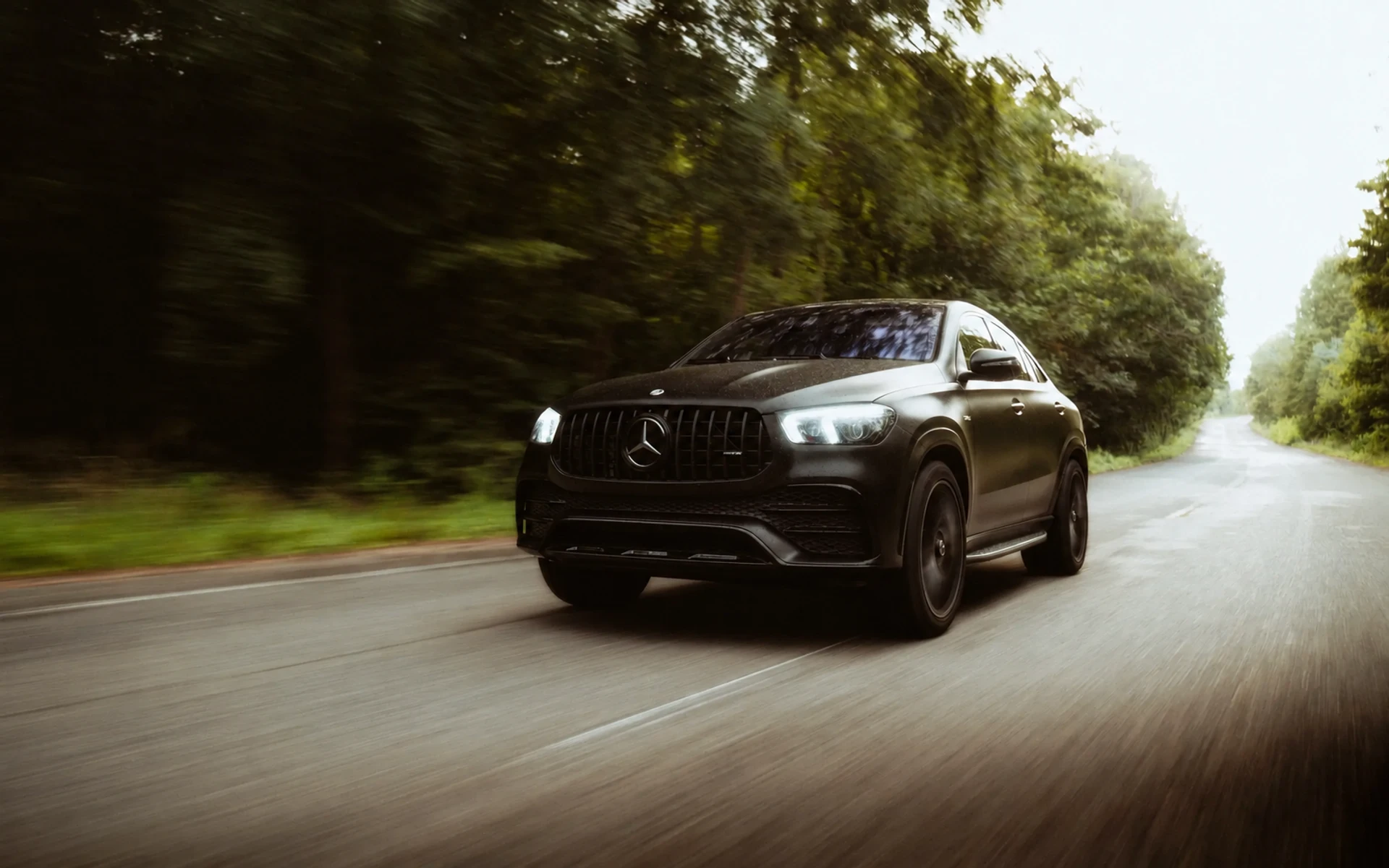 A dark premium SUV travelling at speed along a tree-lined road.
